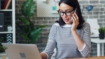 a woman talking on a cell phone while using a laptop