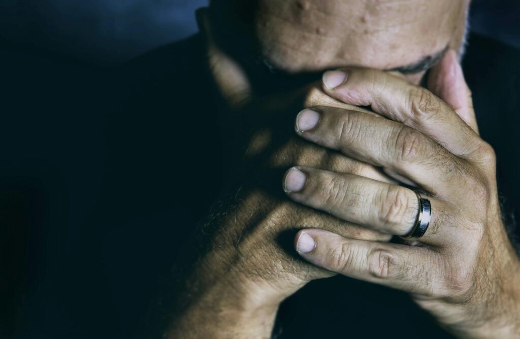 Close-up of an elderly man covering his face, expressing sadness and contemplation.