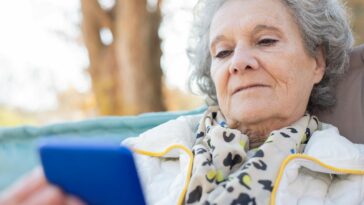 Elderly woman with a smartphone relaxing outdoors in autumn.