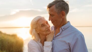 Elderly couple shares a tender moment by a lake during sunset, capturing love and serenity.