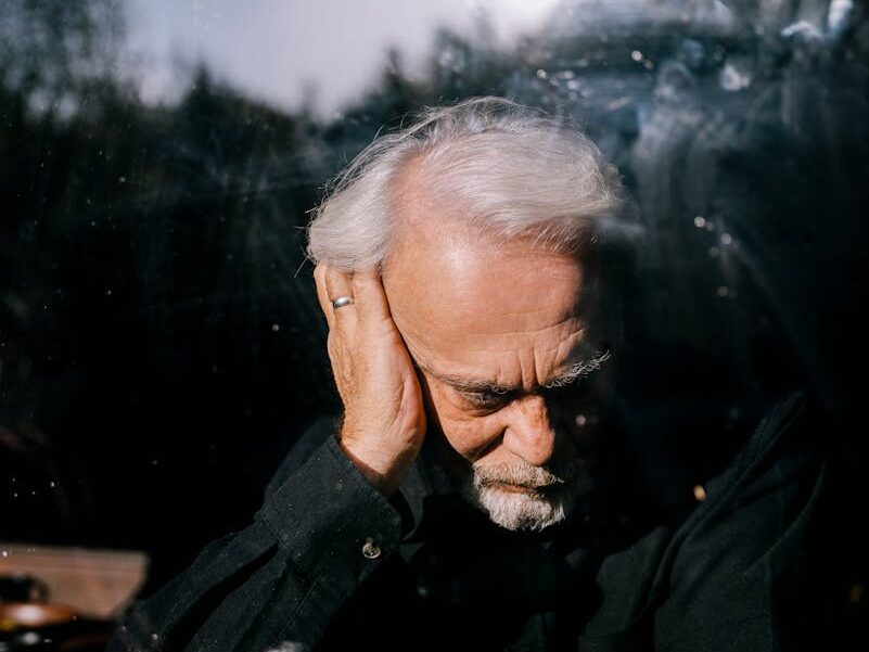 Senior man with hand on head in reflection, expressing grief and contemplation.