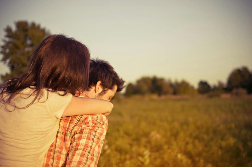 A couple shares a loving embrace during a sunset in a tranquil field.