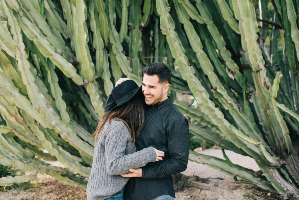 A joyful couple embraces outdoors in front of a large cactus, radiating love and happiness.