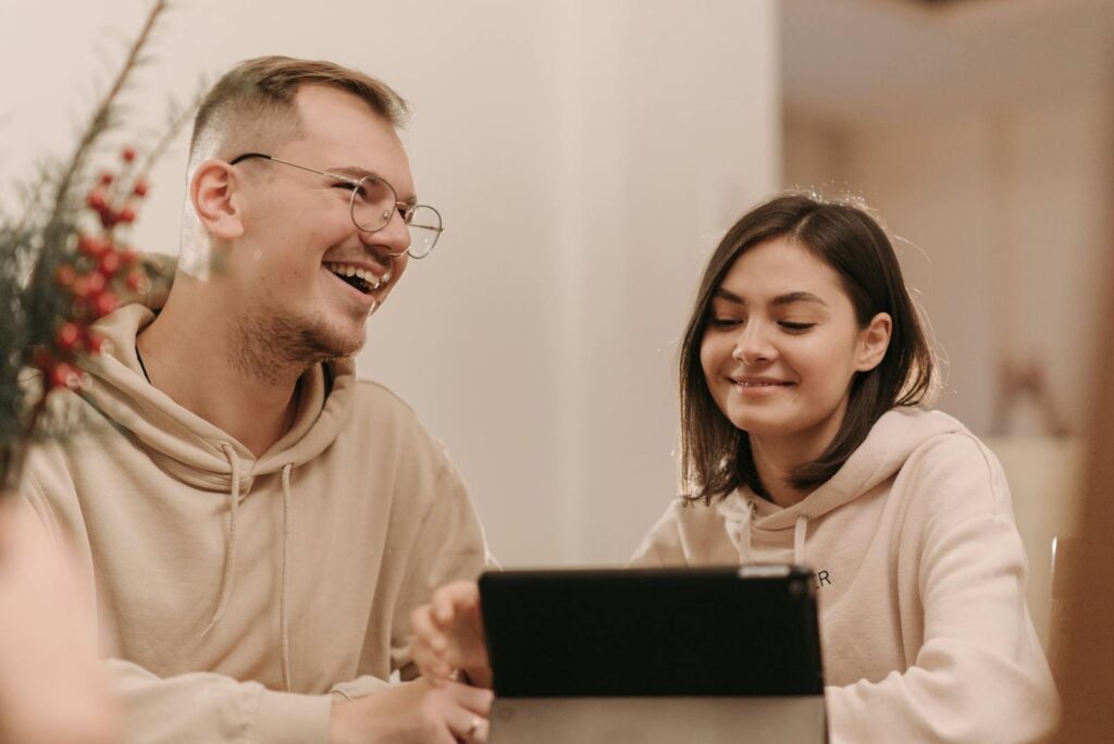 Smiling friends in hoodies enjoying a laugh together indoors, using a tablet.
