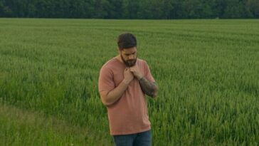 man in brown long sleeve shirt and blue denim jeans standing on green grass field during
