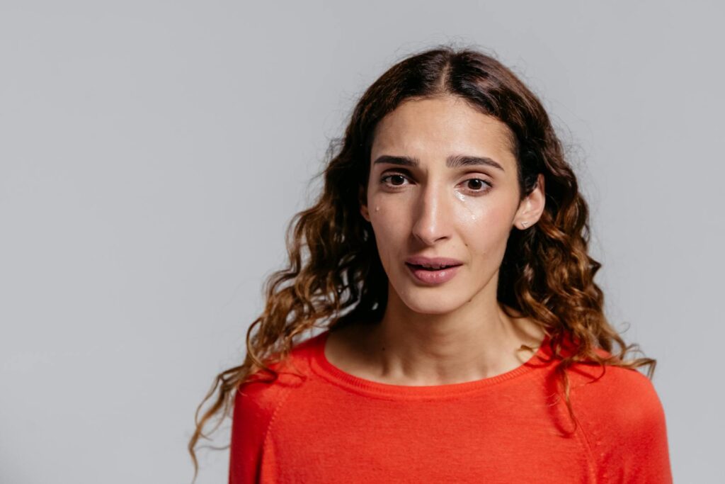 A woman in a studio displaying emotions and tears against a gray background.