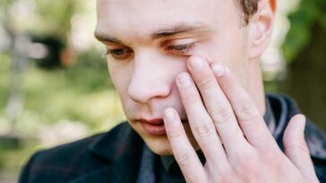 A close-up portrait of a man outdoors, displaying emotions with hand on his face.