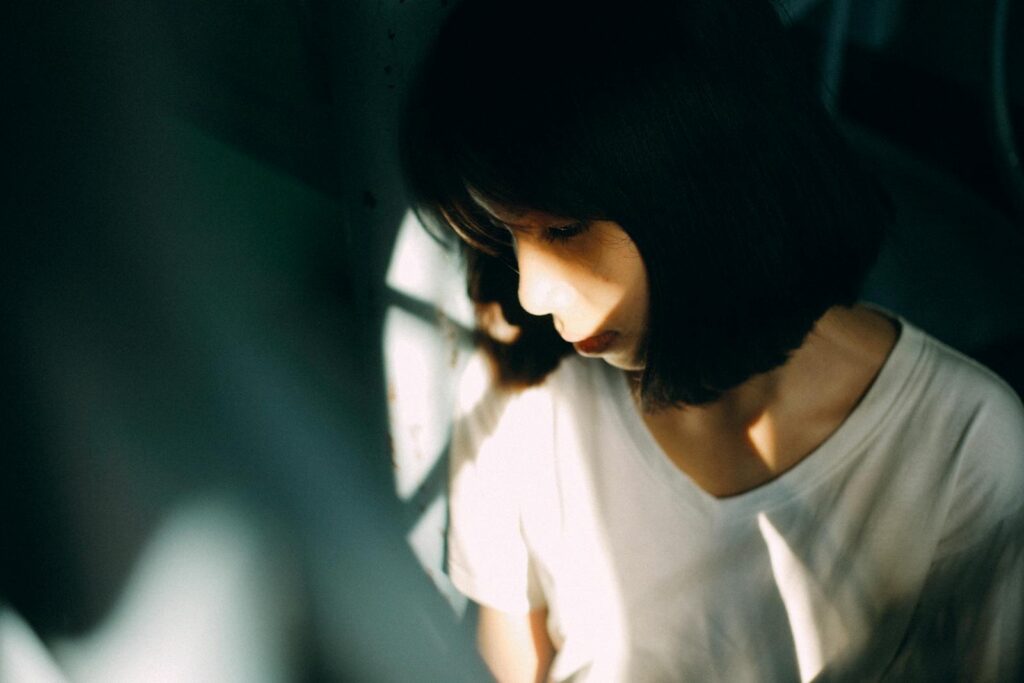 Moody portrait of a woman in soft shadow lighting, conveying deep thought.