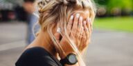 person covering face with hands outdoors