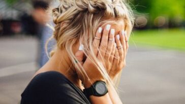 person covering face with hands outdoors