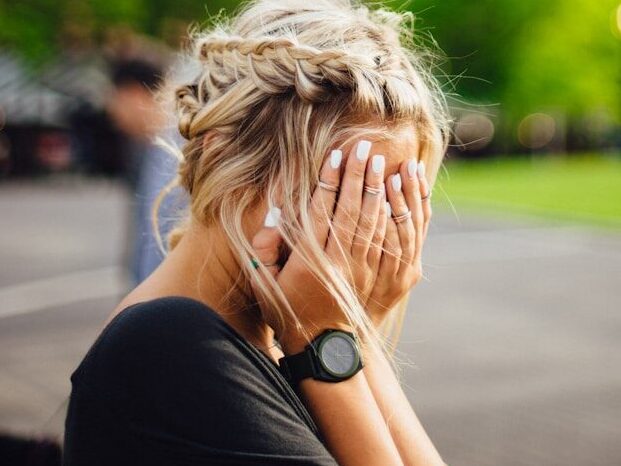 person covering face with hands outdoors