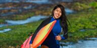 smiling woman carrying surfboard during daytime
