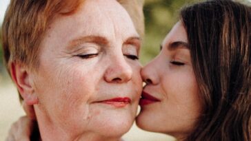 A tender moment of a woman kissing her mother on the cheek outdoors, symbolizing love and connection.