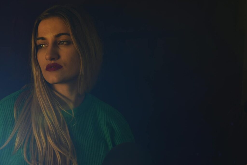 A thoughtful woman in a green sweater looking away in a dark, moody setting. Stylish and expressive.