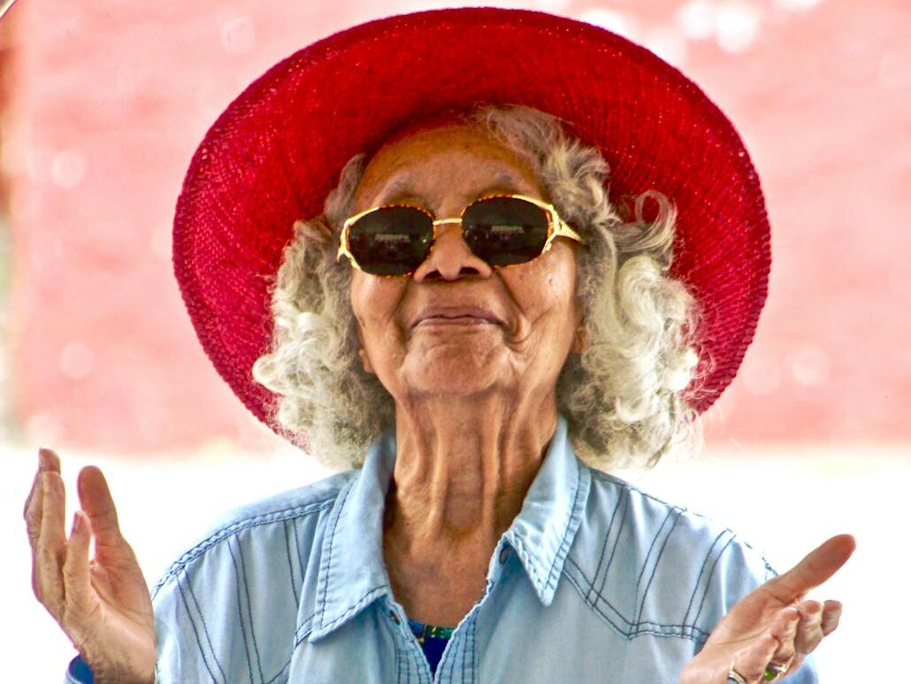 Joyful senior woman wearing a vibrant red hat and sunglasses, expressing happiness outdoors.