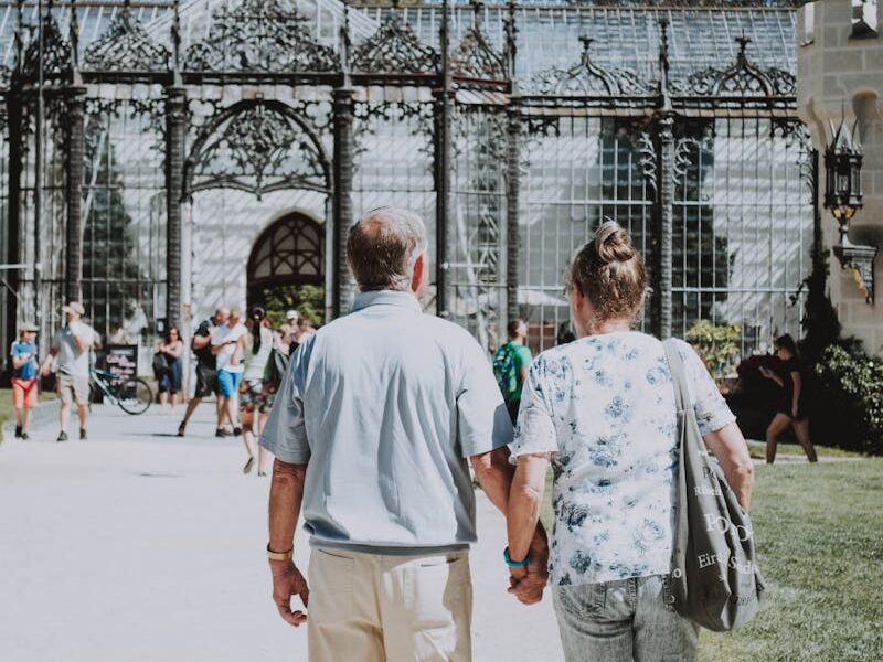 A couple holding hands strolling by a historic gothic-style structure during a sunny day.