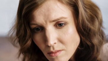 A woman with curly hair in deep thought, indoors, conveying emotion.