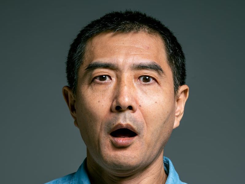 Close-up of a surprised man with open mouth wearing a blue denim shirt.