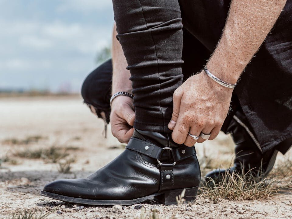 Close-up of a man adjusting his black leather boots outdoors, showcasing modern fashion.