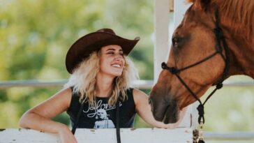 girl in black tank top and blue denim jeans sitting on white wooden fence beside brown