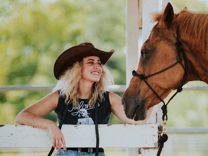 girl in black tank top and blue denim jeans sitting on white wooden fence beside brown