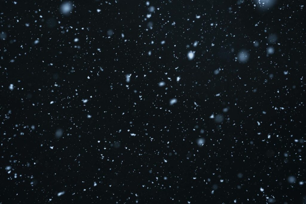 A mesmerizing view of snowflakes falling against a dark, starry night sky.