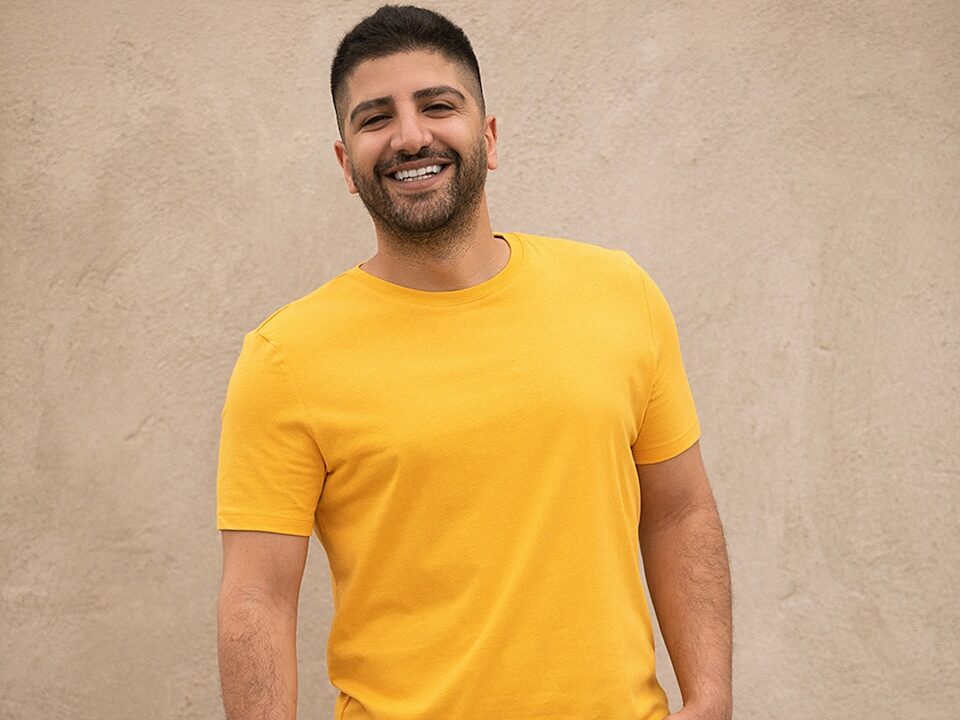 man in yellow crew neck t-shirt and black denim jeans standing beside white wall