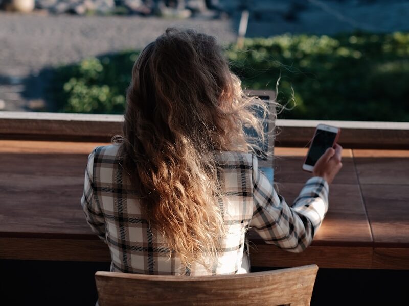 woman in white and black plaid shirt holding black smartphone