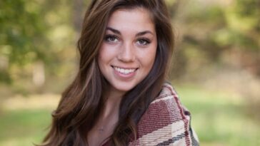 A woman smiling outdoors with a cozy plaid shawl, surrounded by nature in a sunny park.