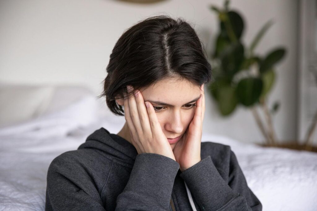 Woman sitting indoors in thought, wearing a hoodie. Expressions of contemplation and introspection.