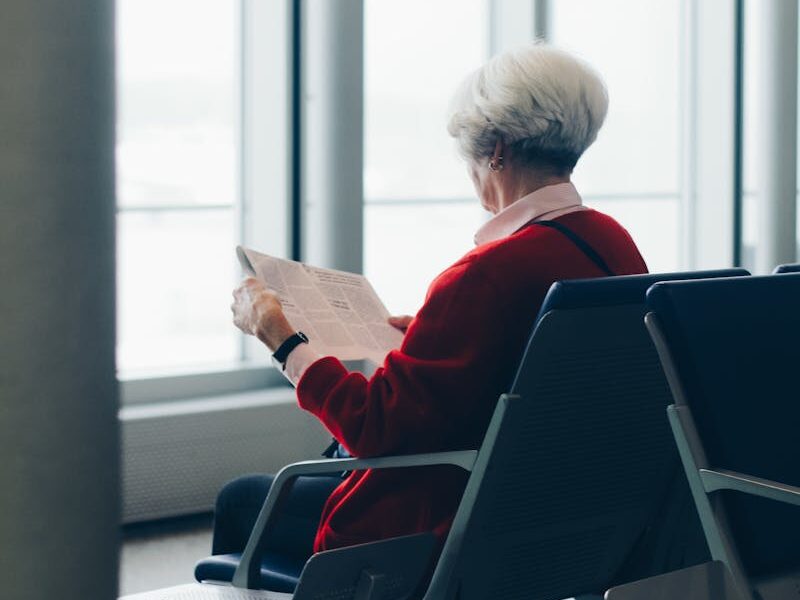 Elderly woman reading newspaper while seated at an airport gate.