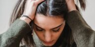 A woman sitting indoors, appearing stressed or upset, touching her head.