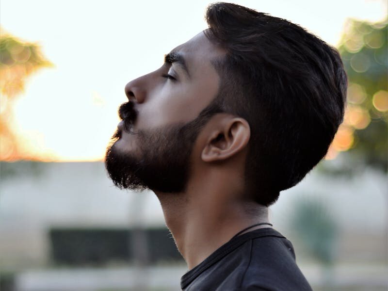 Side view portrait of a bearded man gazing upwards in an outdoor setting with blurred background.