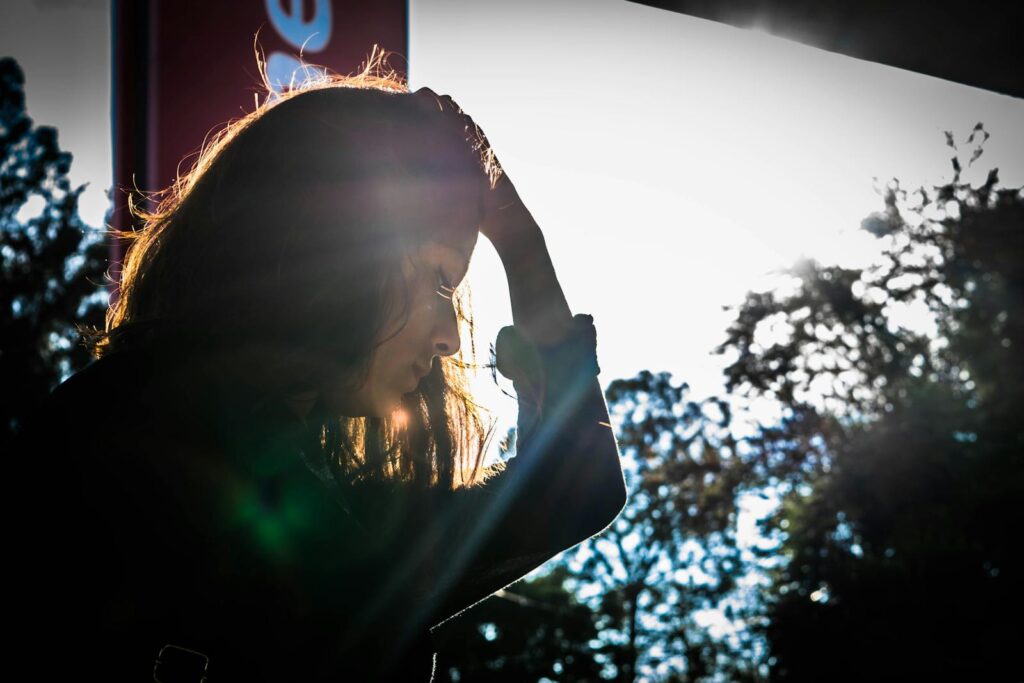 A silhouette of a woman touching her head, surrounded by nature and sunlight.