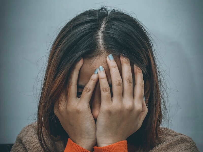 woman in brown sweater covering her face with her hand