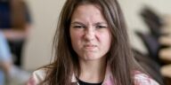 An angry teenage girl sitting in a classroom, displaying a frustrated expression.