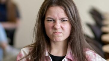 An angry teenage girl sitting in a classroom, displaying a frustrated expression.
