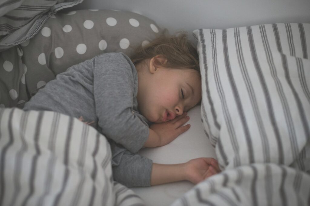 baby in gray long sleeve shirt lying on white and black stripe bed
