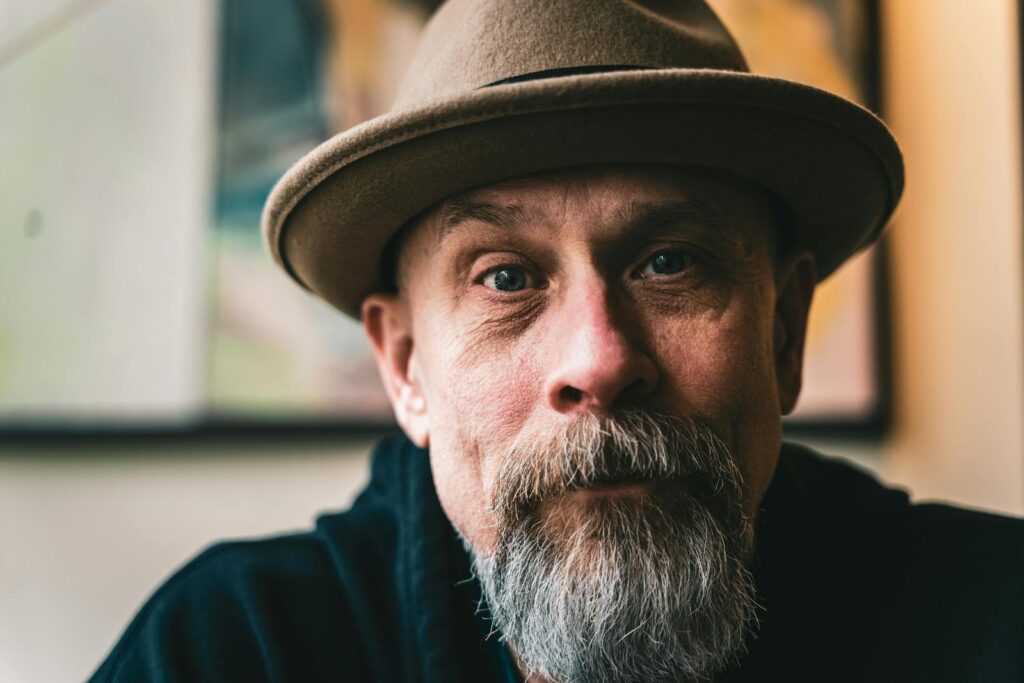 Close-up portrait of a mature man with a beard wearing a fedora hat, evoking a vintage style.