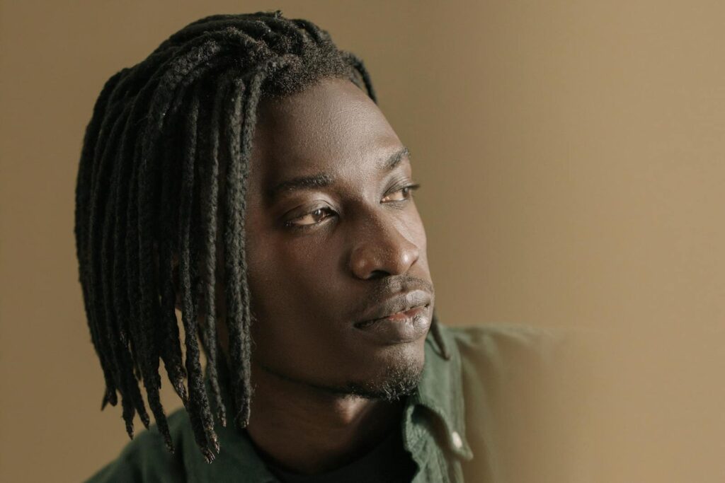 Close-up portrait of a young man with braided hair looking away, showing thoughtful expression.