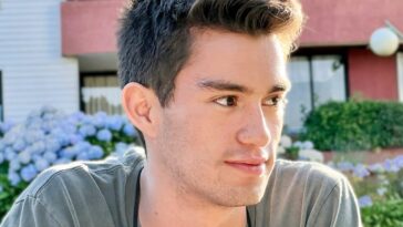 a man with a short haircut sitting in front of a building
