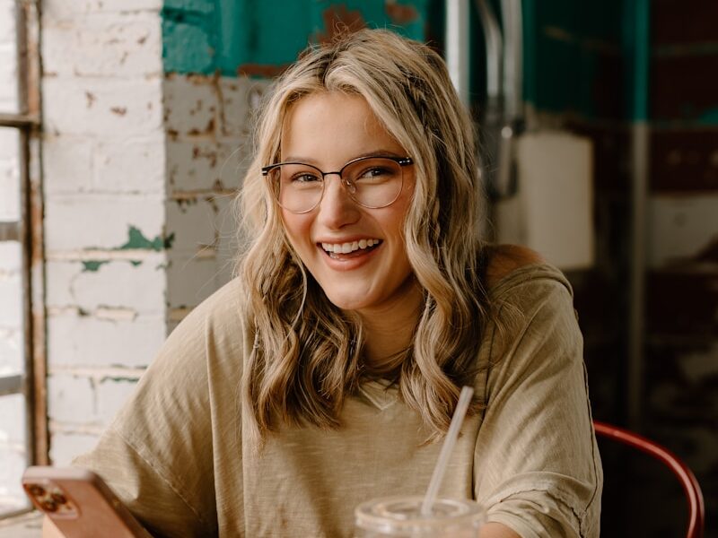 a woman sitting at a table with a drink and cell phone