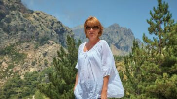 woman in white blouse wearing sunglasses standing on mountain during daytime