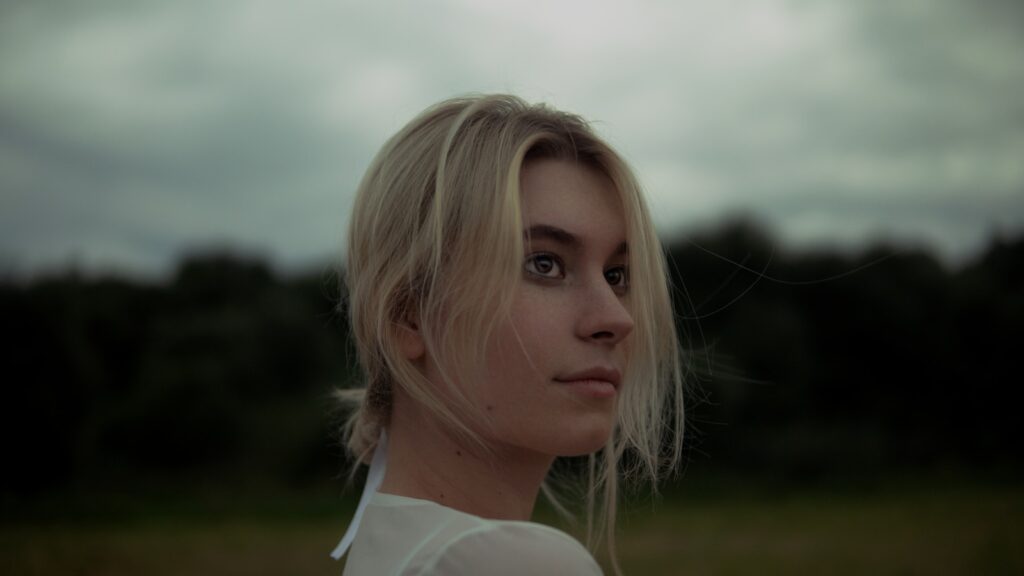 a woman standing in a field with trees in the background